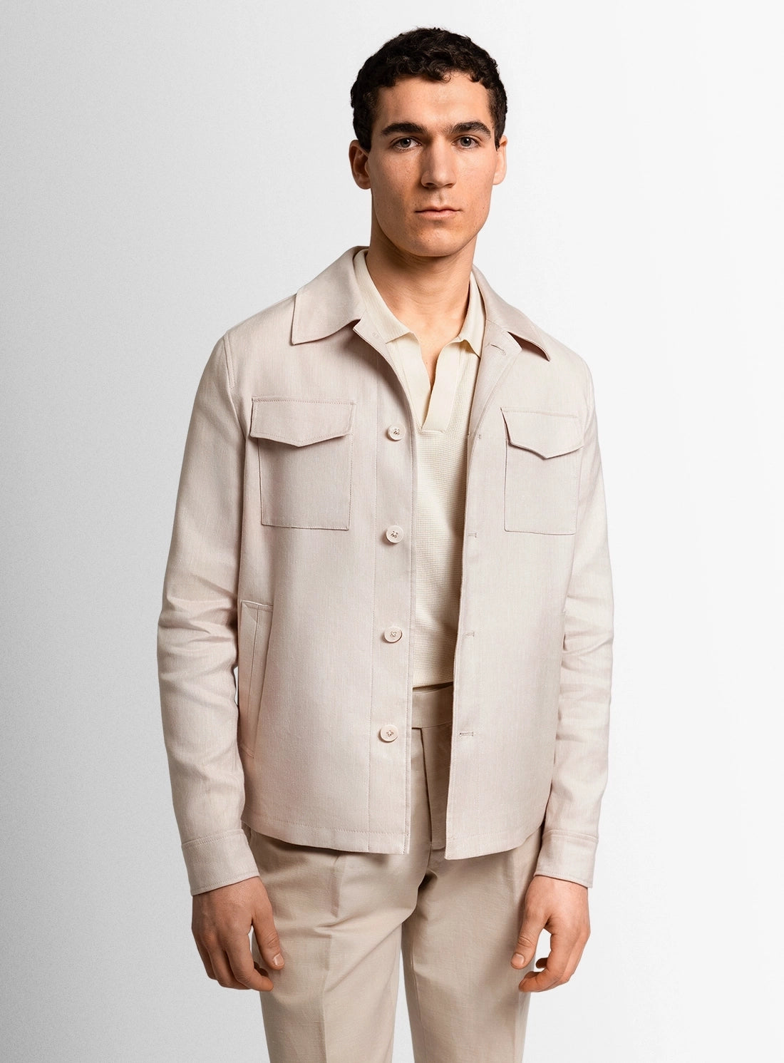 Man wearing a beige jacket and pants against a light gray background