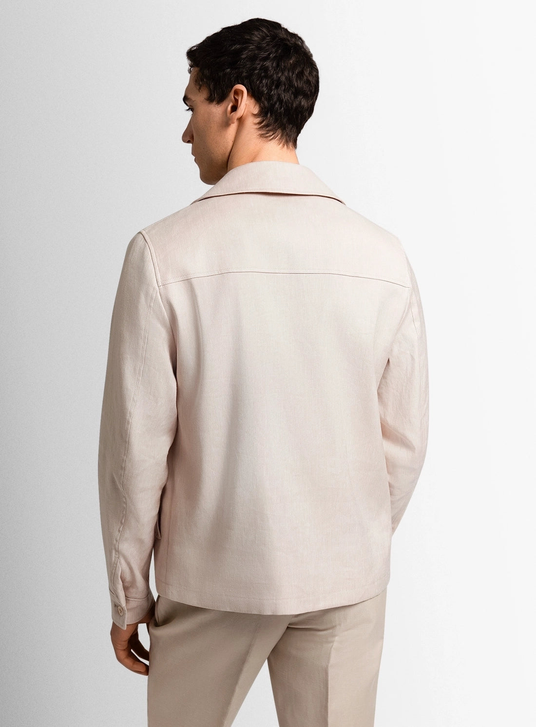 Man wearing a beige jacket and pants on a plain background