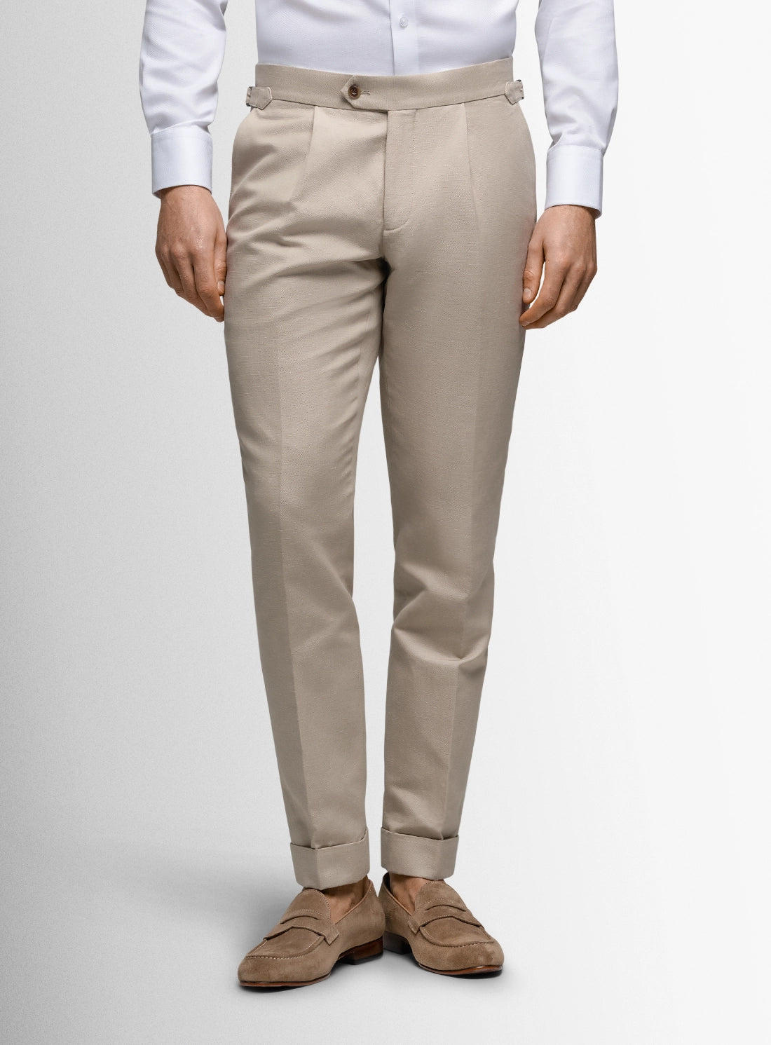 Beige pants worn with a white shirt and brown shoes on a plain background
