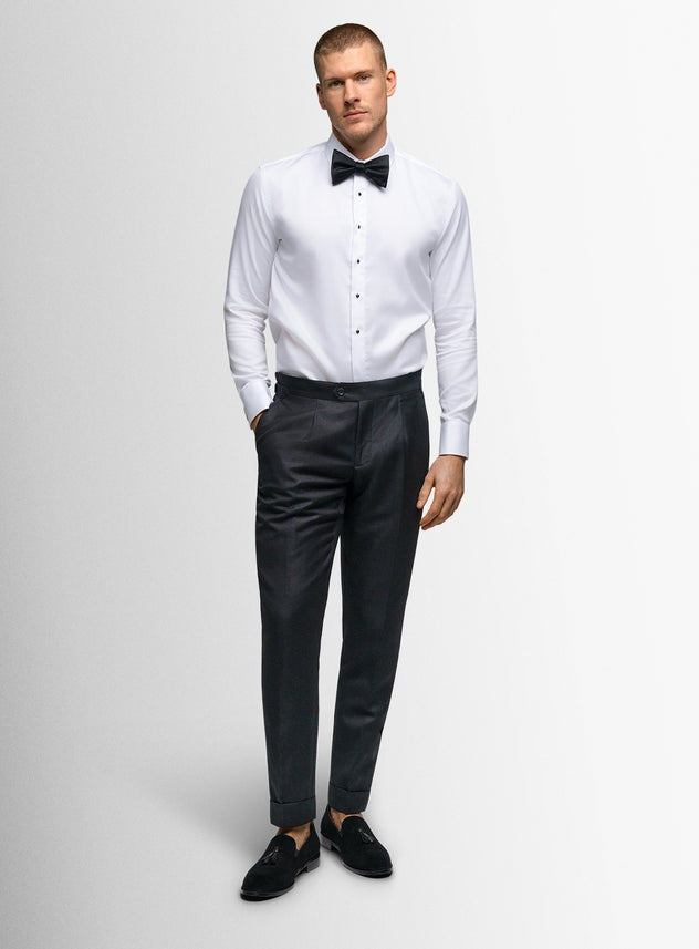 Man wearing a white dress shirt with black bow tie and black pants on a light gray background