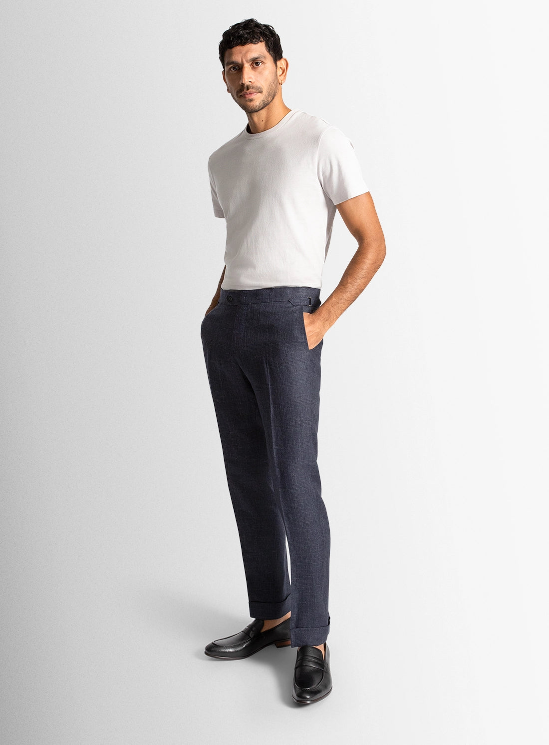 Man wearing a white t-shirt and dark pants on a light gray background