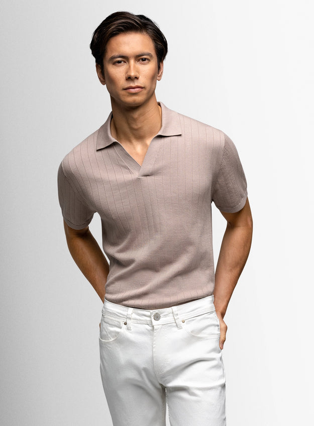 Man wearing a beige polo shirt and white pants against a light gray background