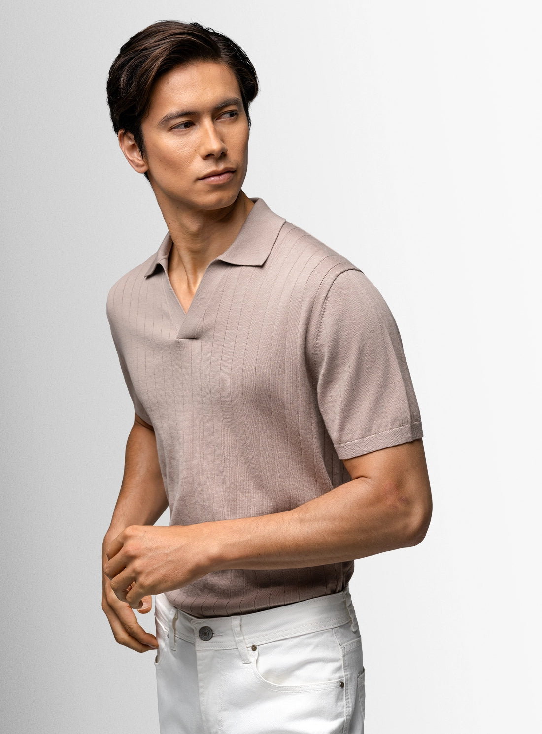 Man wearing a light brown polo shirt and white pants against a gray background