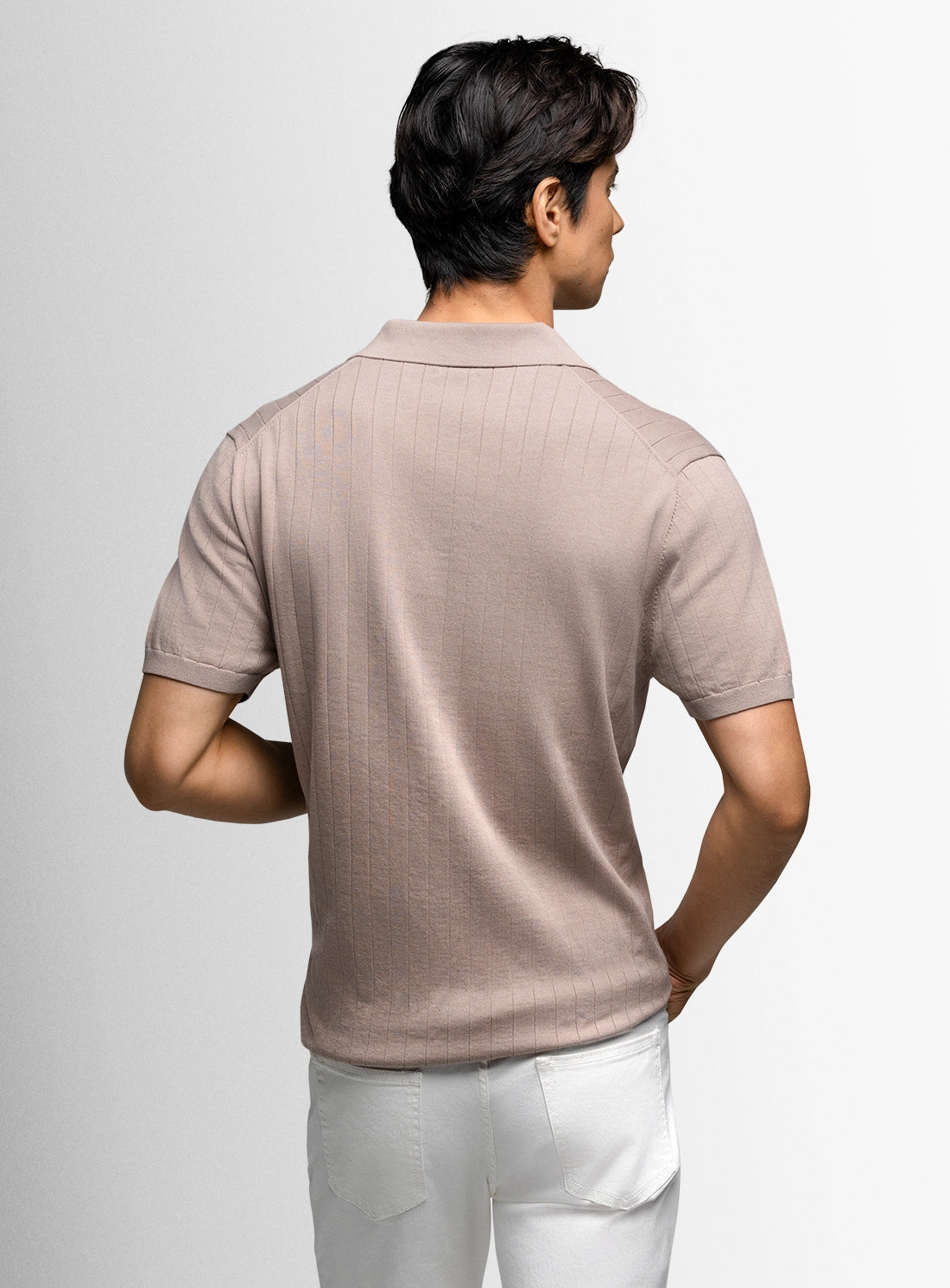 Man wearing a beige polo shirt and white pants on a light gray background
