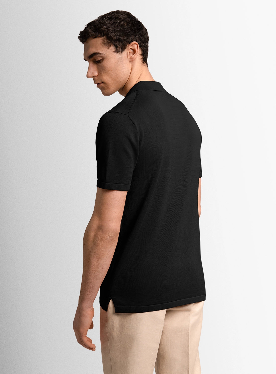 Man wearing a black polo shirt and beige pants on a light gray background