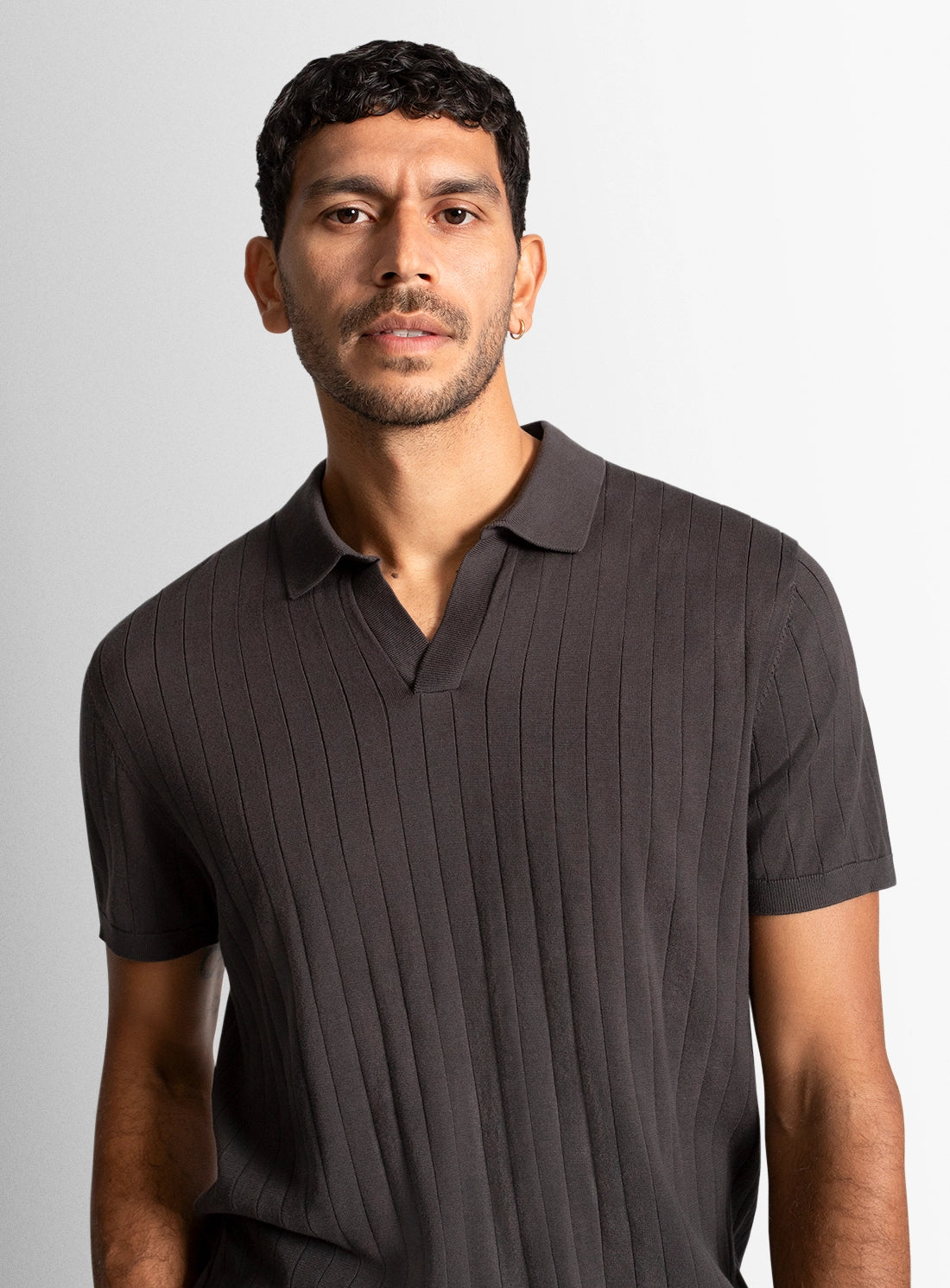 Man wearing a dark brown ribbed polo shirt against a plain background