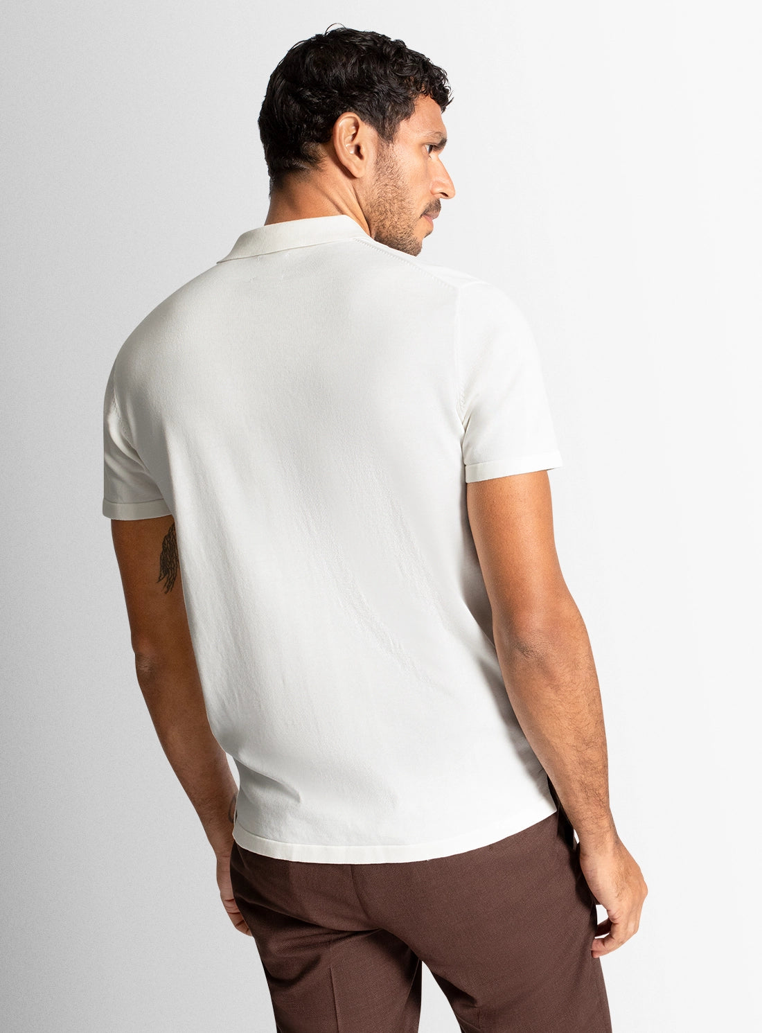 Man wearing a white polo shirt and brown pants on a light gray background