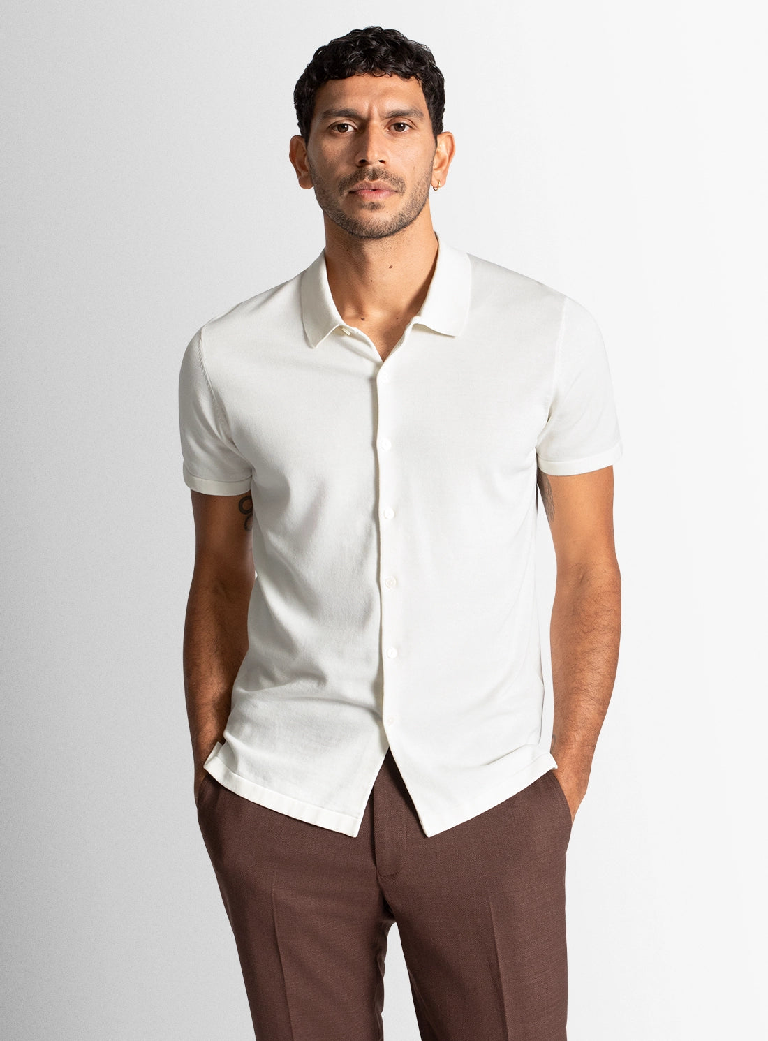 Man wearing a white short-sleeve shirt and brown pants against a light gray background