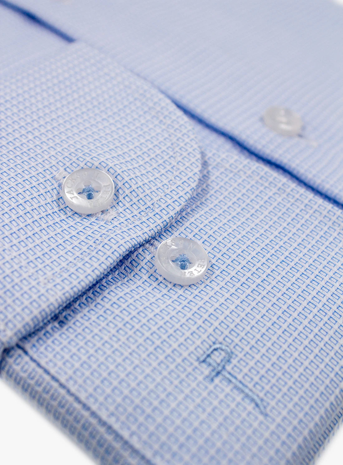 Close-up of a light blue dress shirt with white buttons on a white background