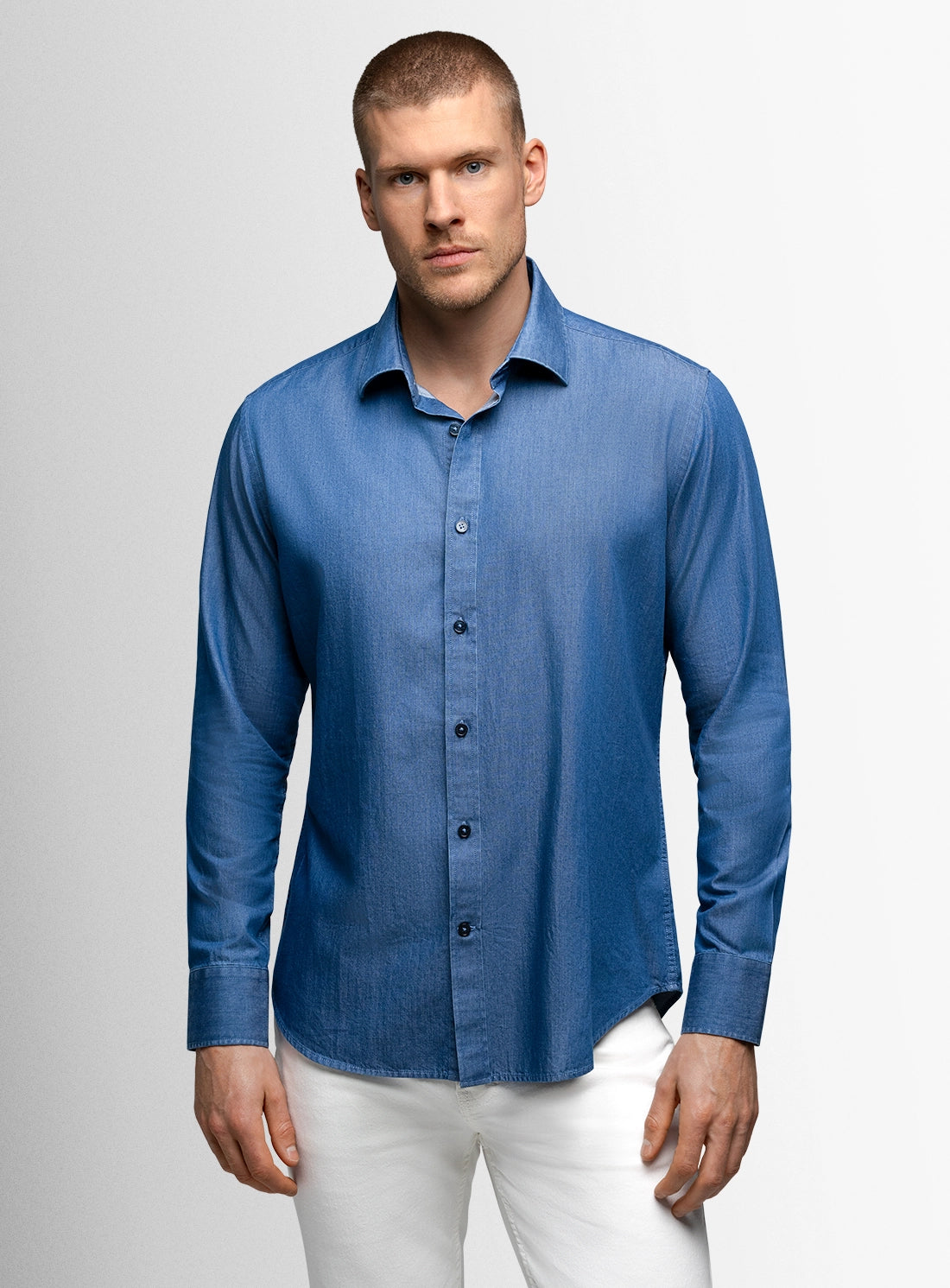 Man wearing a blue shirt and white pants against a gray background