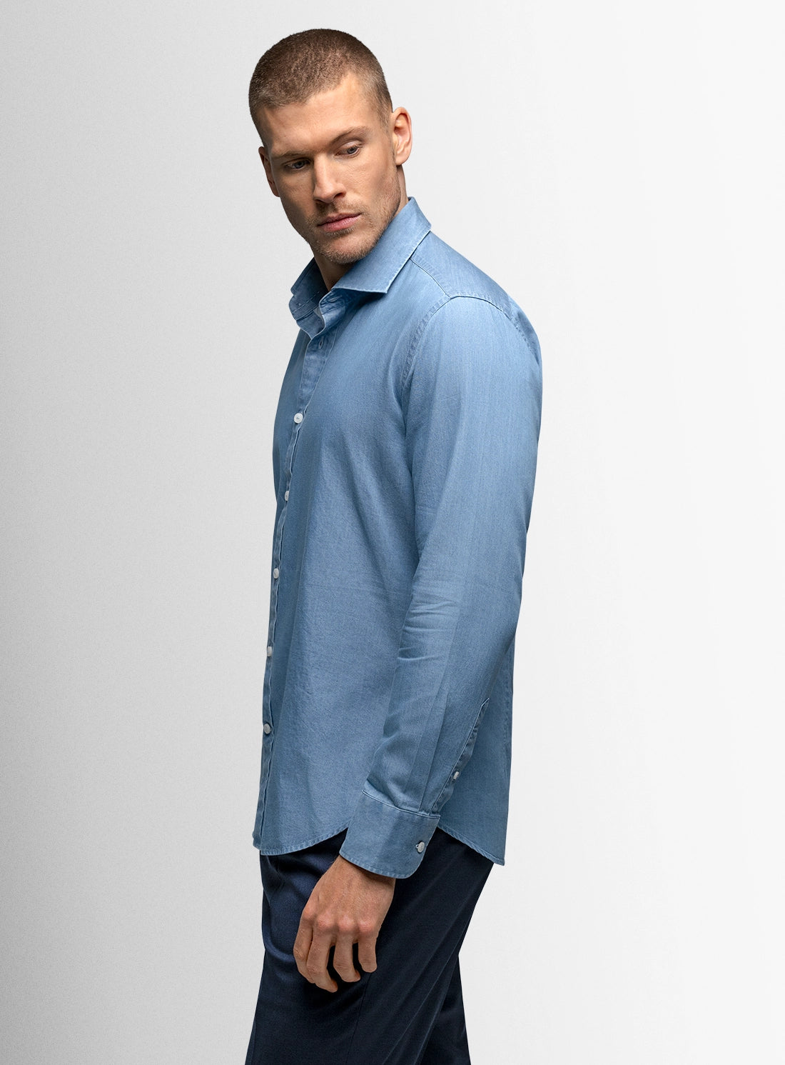 Man wearing a light blue button-up shirt on a gray background