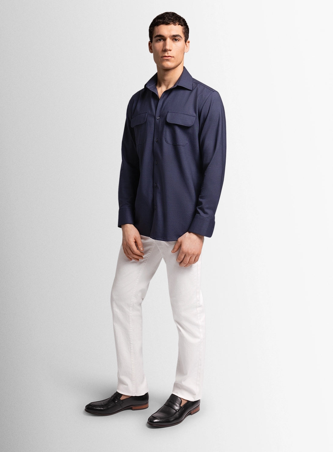 Man wearing a navy shirt, white pants, and black shoes on a light gray background