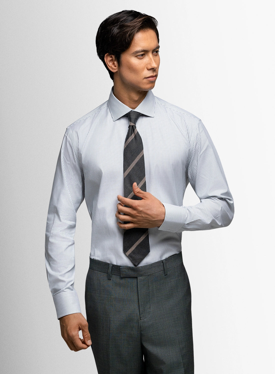 Man wearing a light blue dress shirt, gray tie, and dark gray pants against a plain background