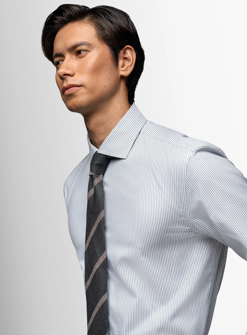 Man wearing a light blue striped shirt and dark tie against a plain background