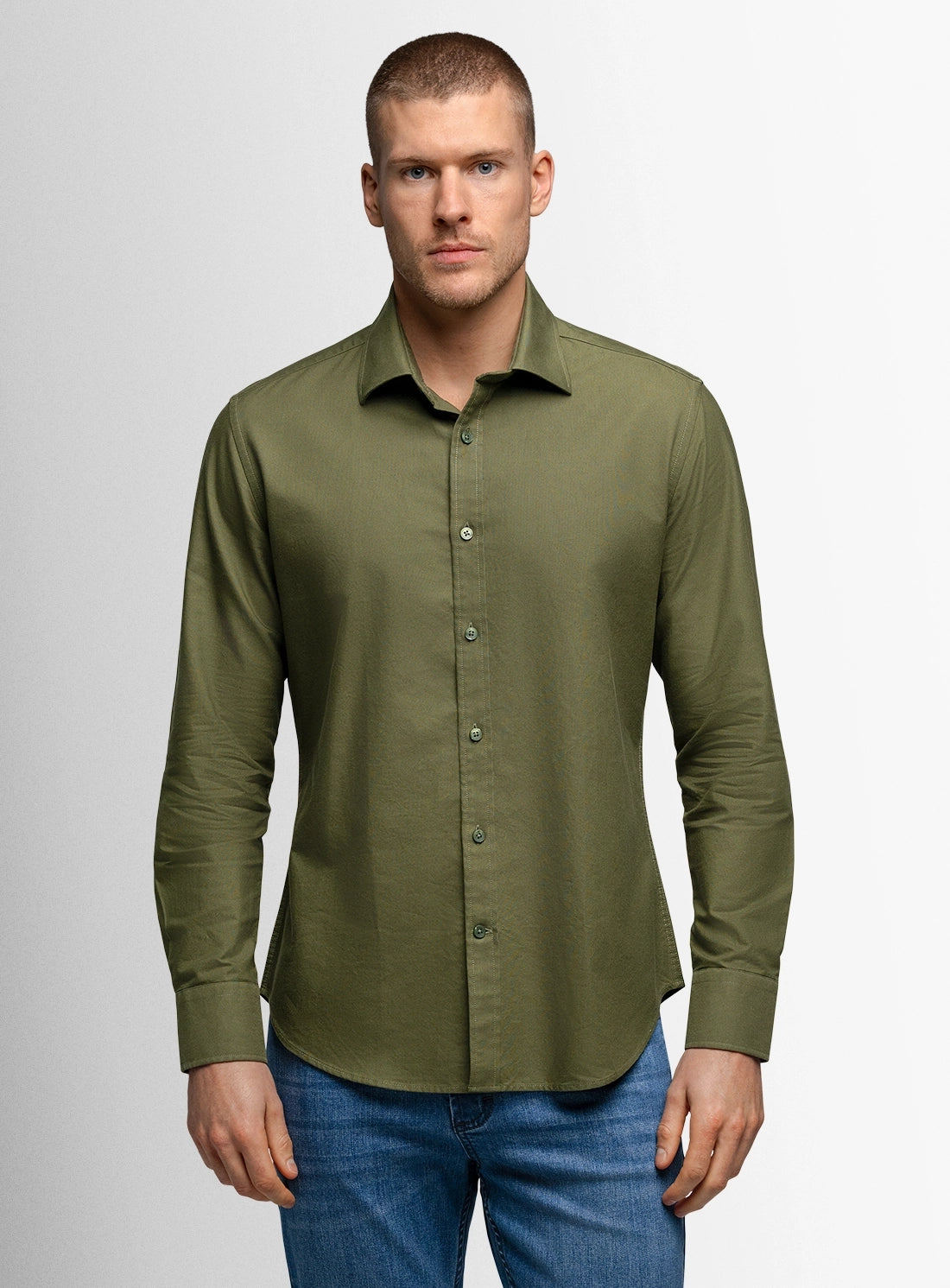 Man wearing a green button-up shirt and blue jeans on a gray background