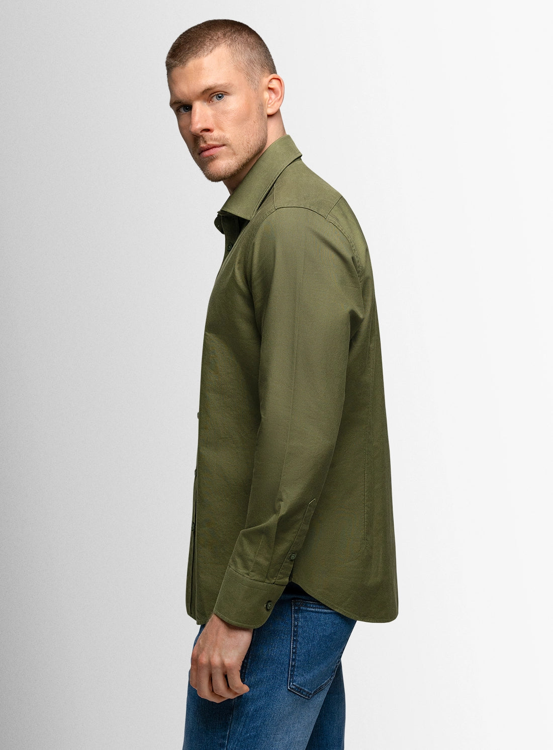 Man wearing a green shirt and blue jeans on a light gray background