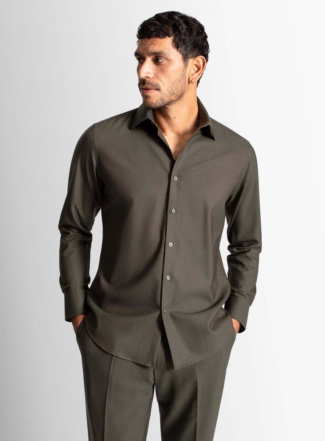 Man wearing a dark green shirt and pants on a gray background