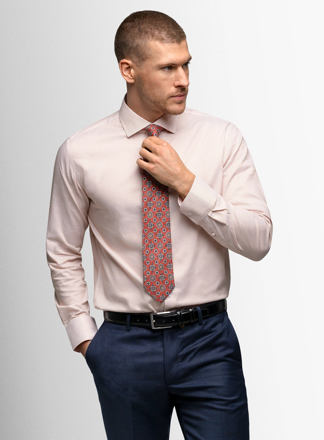 Man adjusting his pink dress shirt and patterned tie against a light gray background