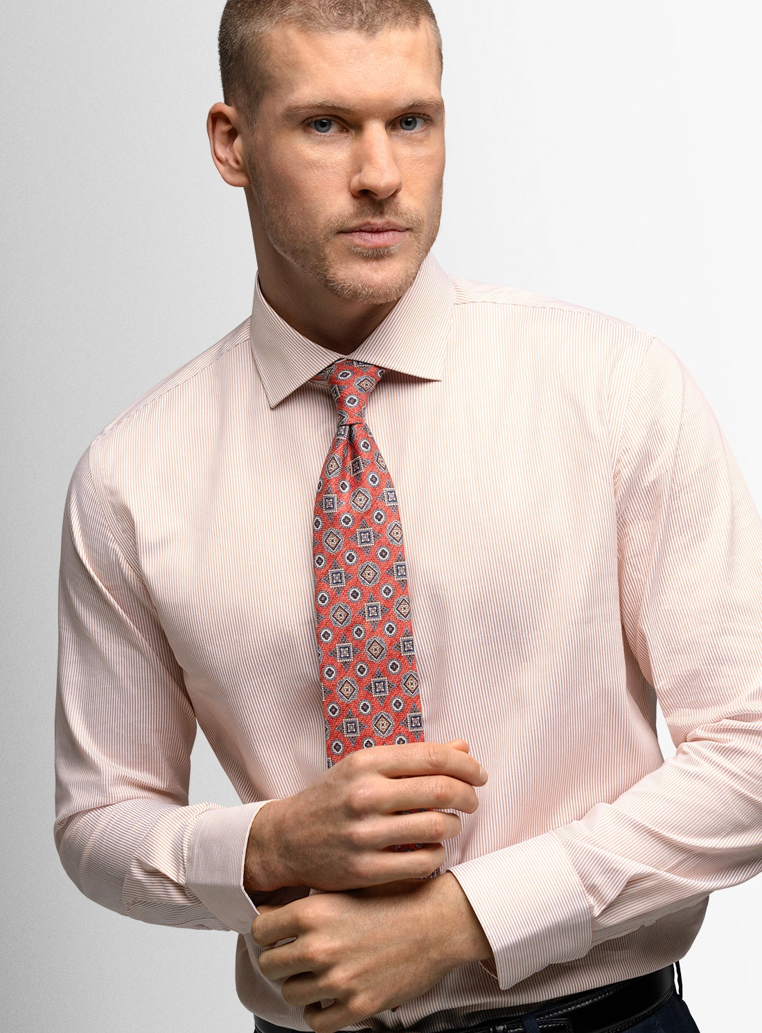 Man wearing a light pink shirt and patterned tie against a plain background