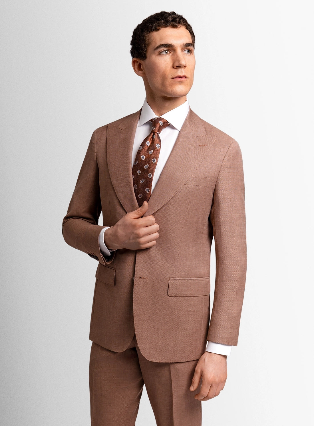 Man wearing a brown suit with a patterned tie on a light gray background