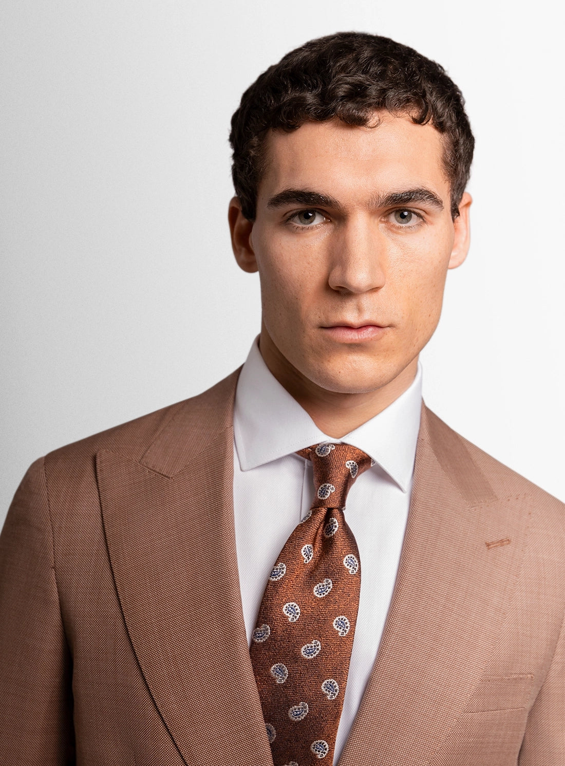 Man wearing a brown suit with a patterned tie on a plain background