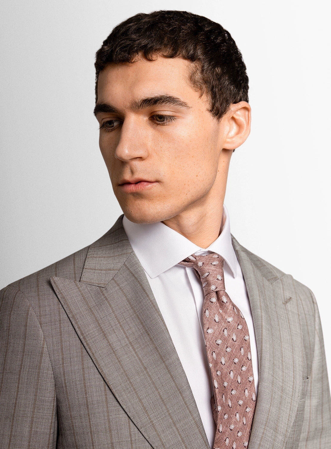 Man wearing a gray suit with a white shirt and patterned tie on a plain background