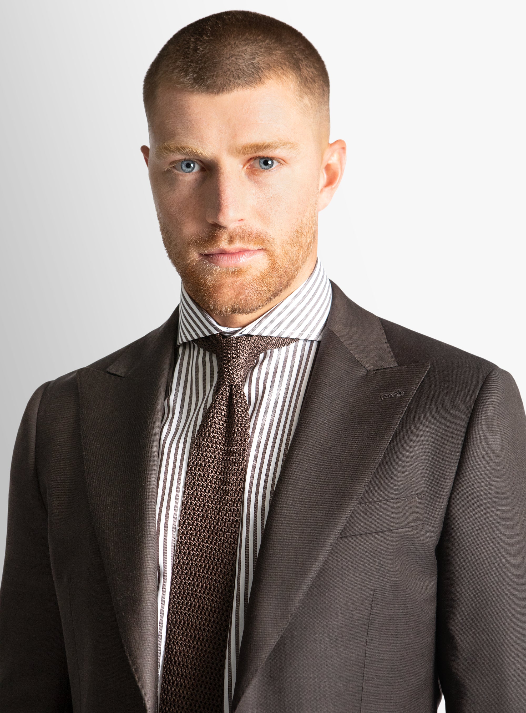 Man wearing a dark suit with a striped shirt and patterned tie on a light gray background