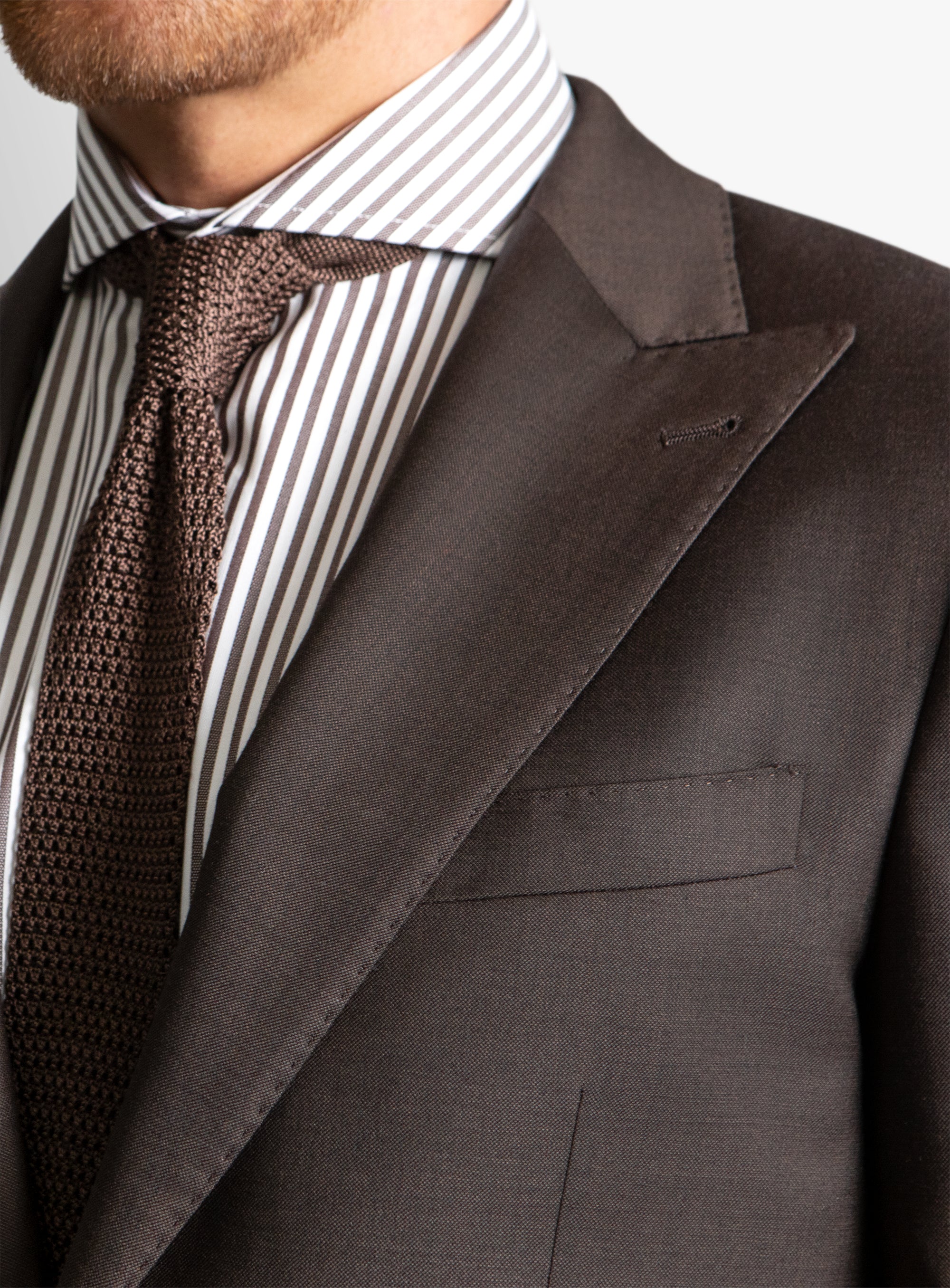 Close-up of a gray suit jacket with a striped shirt and brown tie.