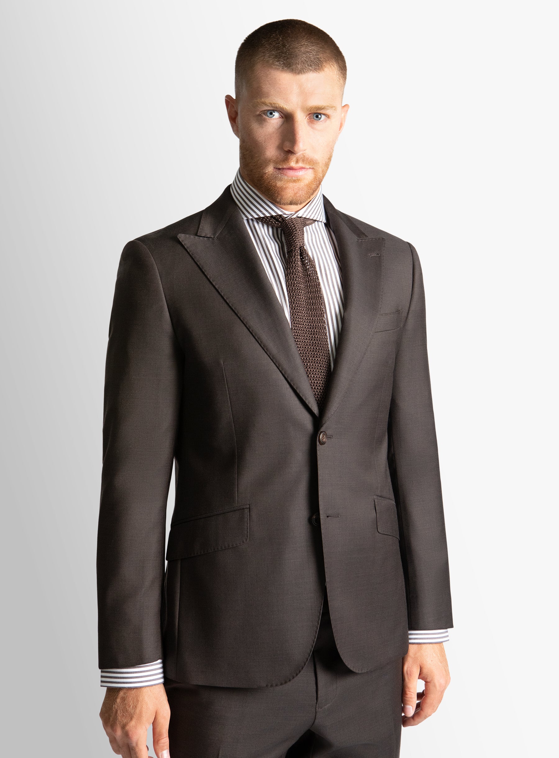Man wearing a brown suit with a striped shirt and tie on a light gray background