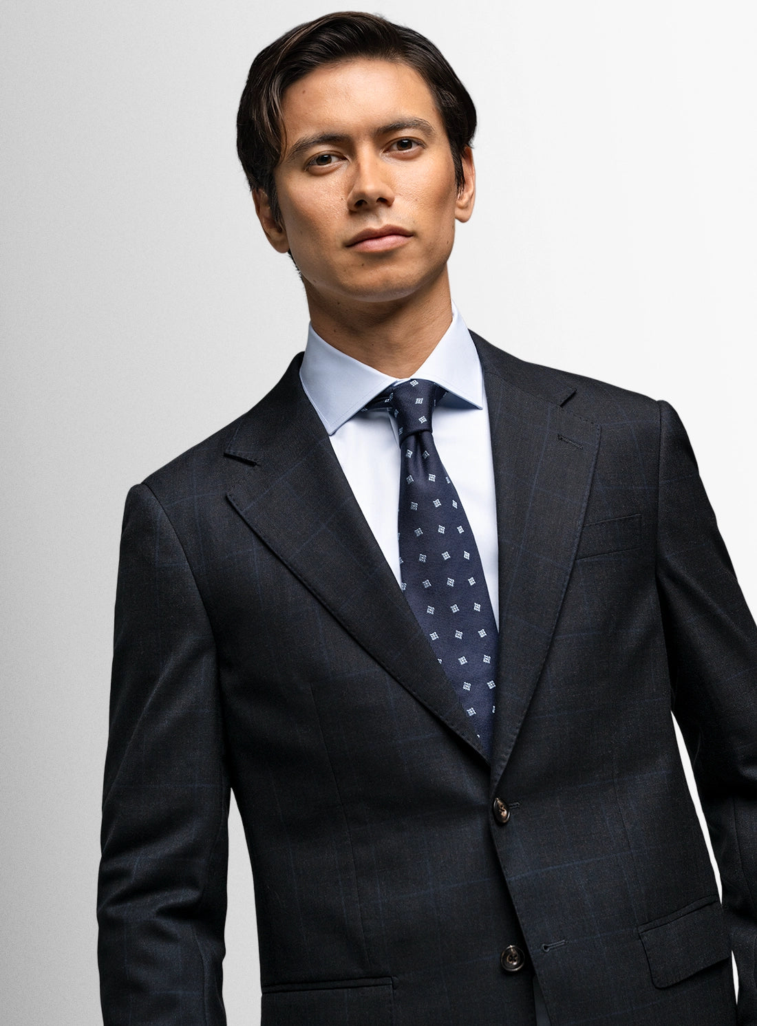Man wearing a dark suit with a light shirt and patterned tie on a plain background
