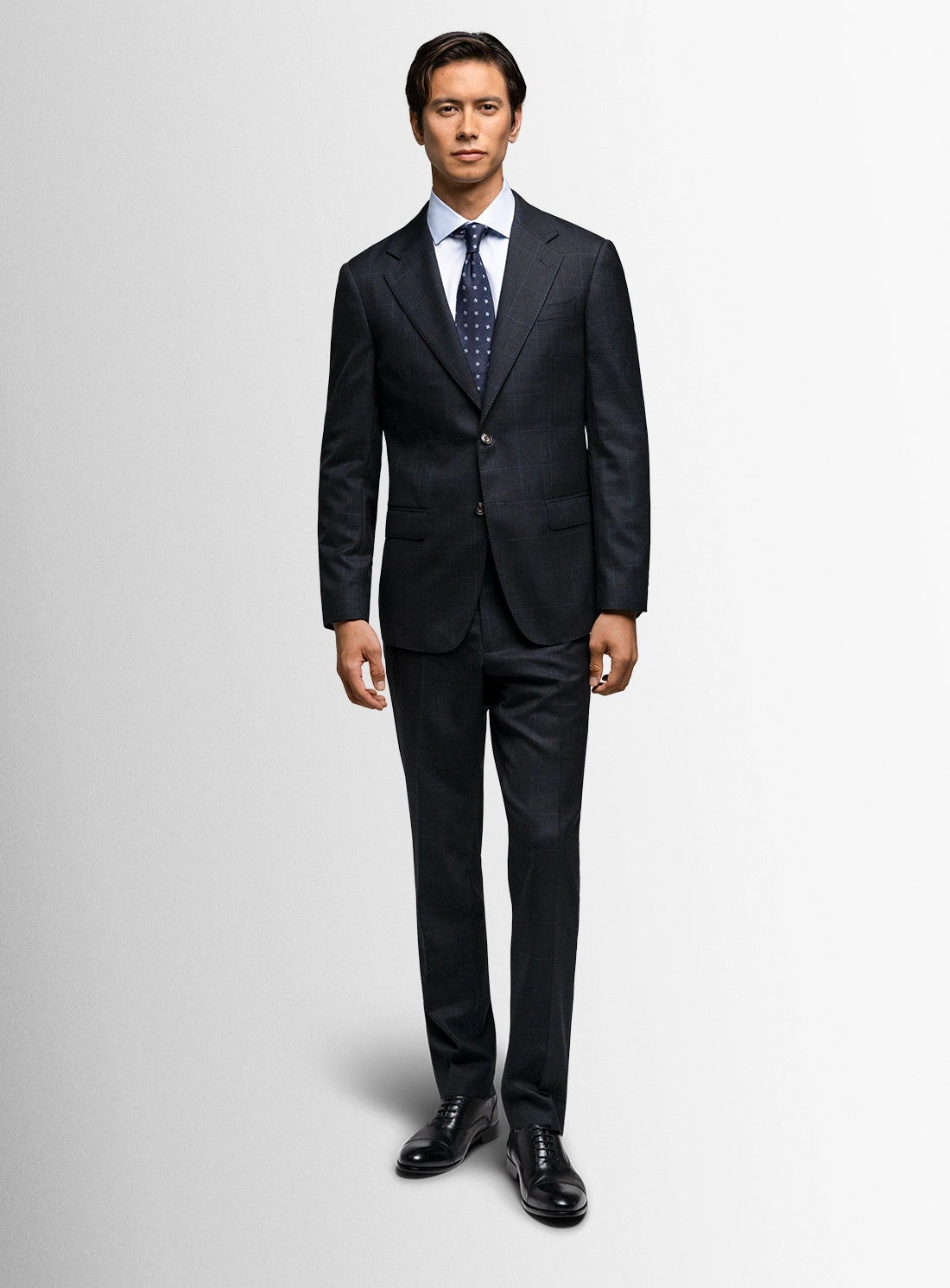 Man wearing a dark gray suit with a white shirt and patterned tie on a light gray background