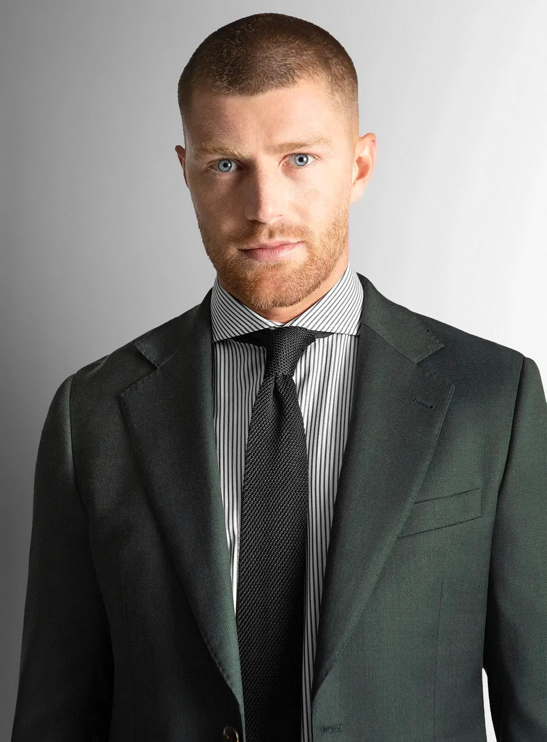 Close up of a man wearing a dark green suit with a striped shirt
