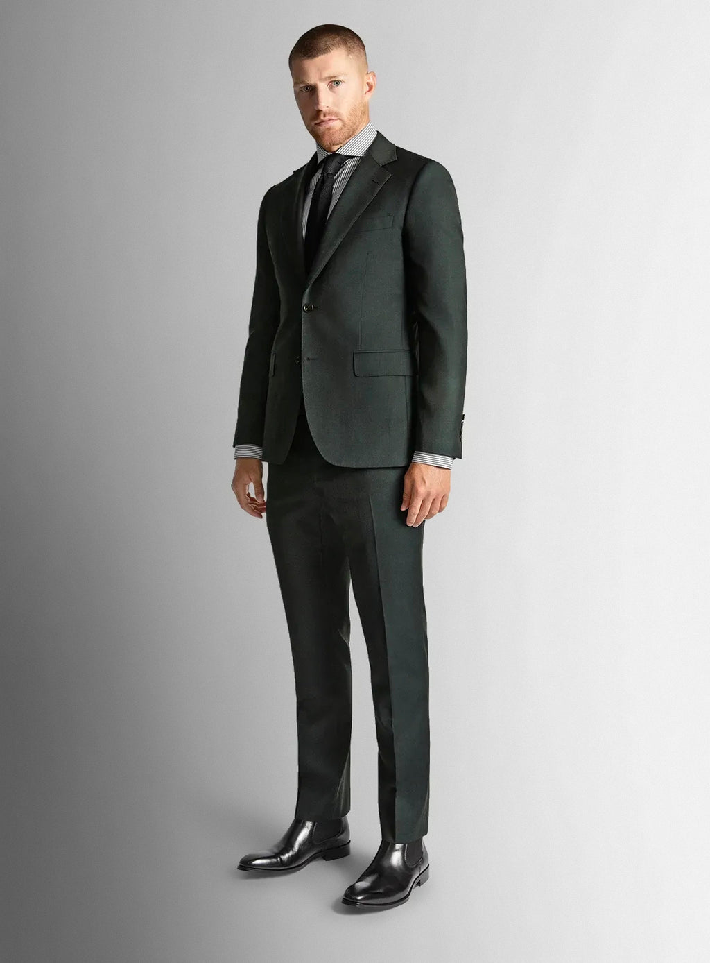 Man wearing a dark green suit with a striped shirt and black shoes