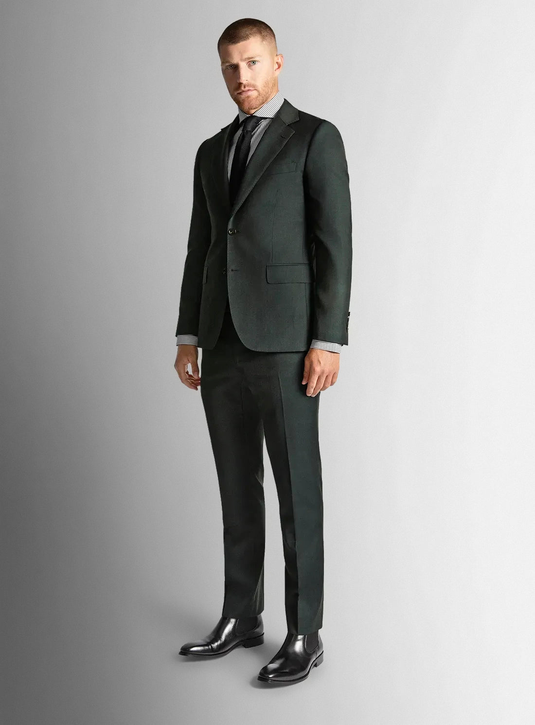 Man wearing a dark green suit with a striped shirt and black shoes