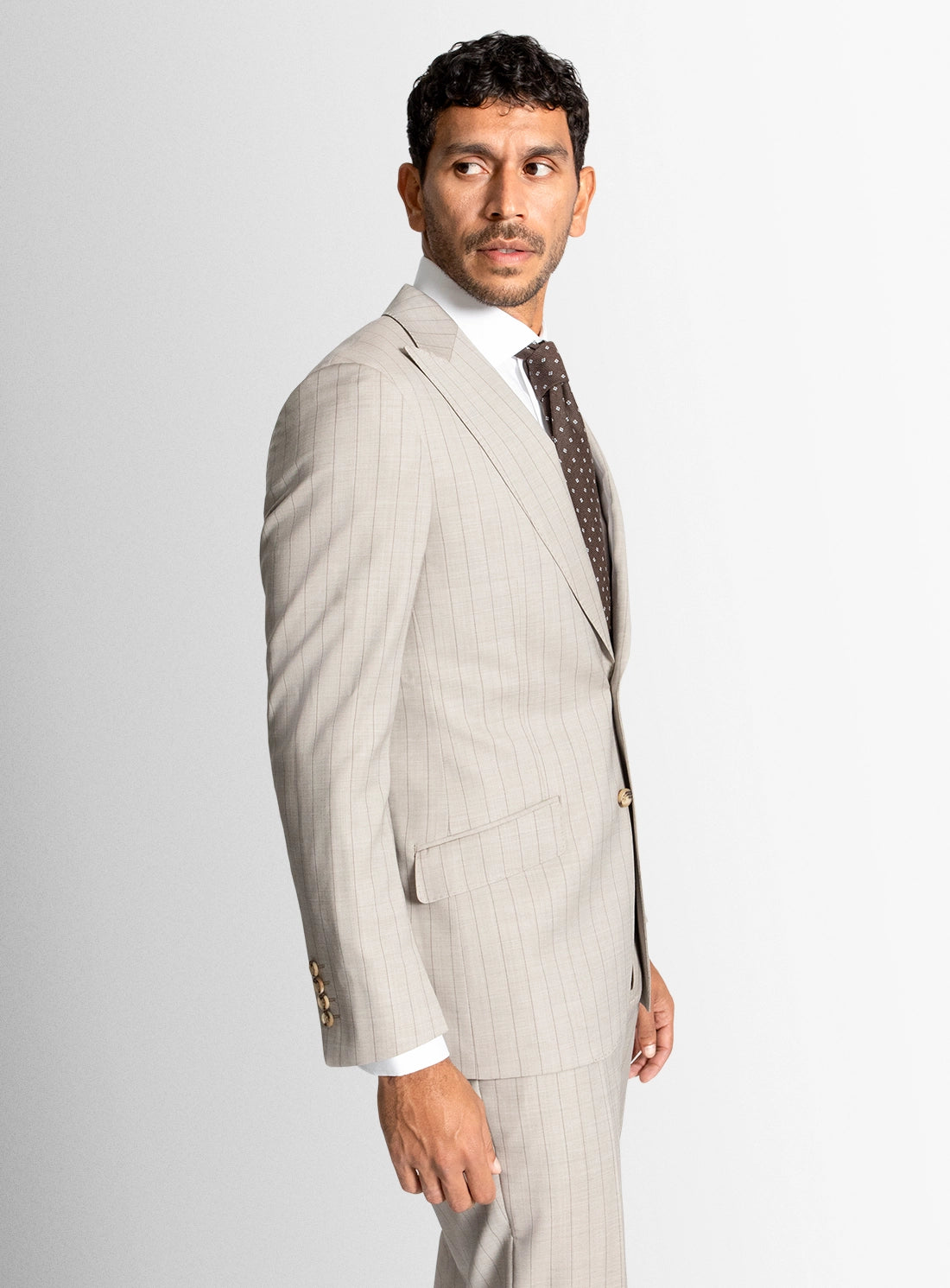 Man wearing a light gray pinstripe suit with a white shirt and patterned tie on a plain background