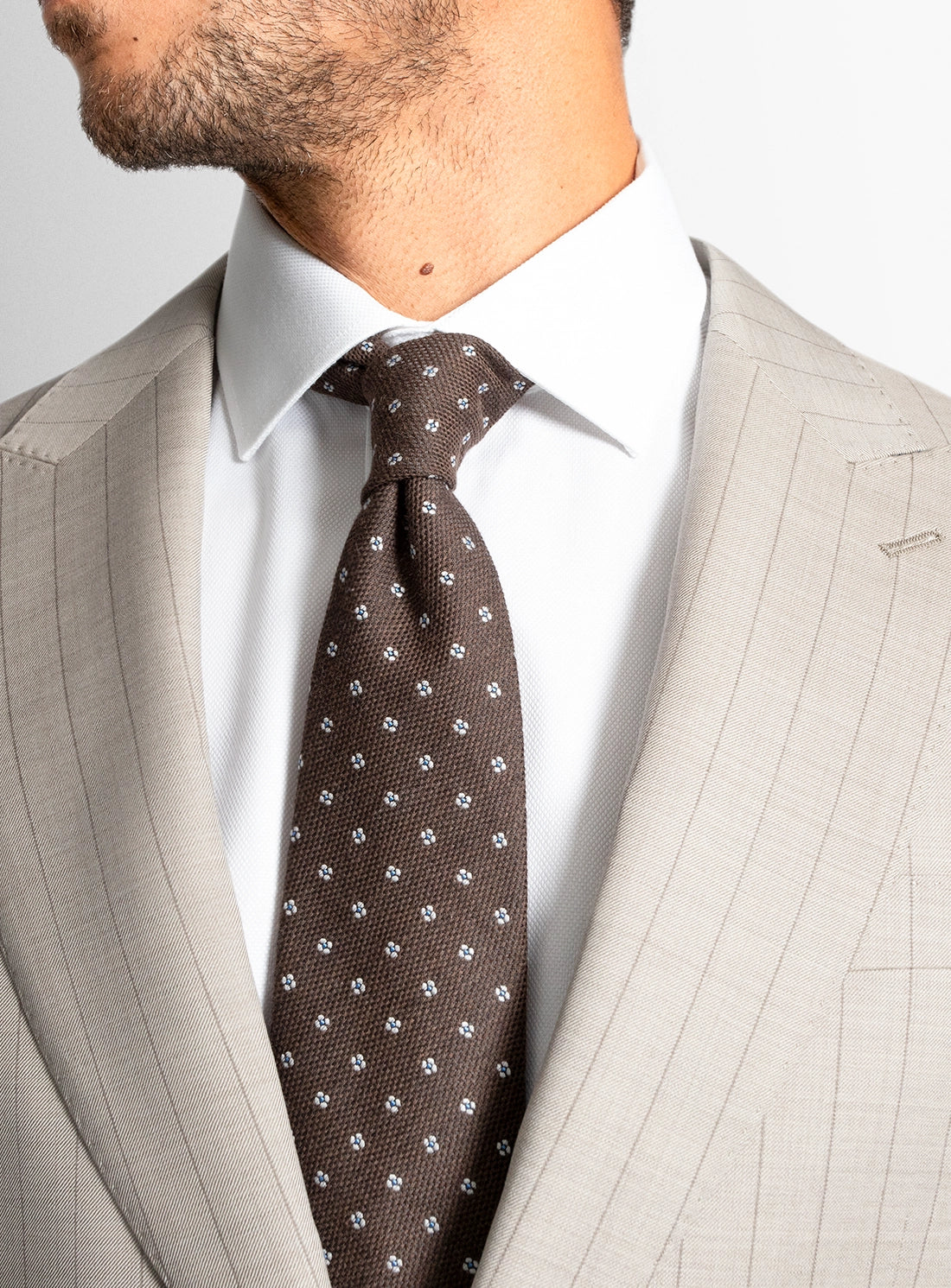 Man wearing a beige suit with a brown patterned tie against a light gray background