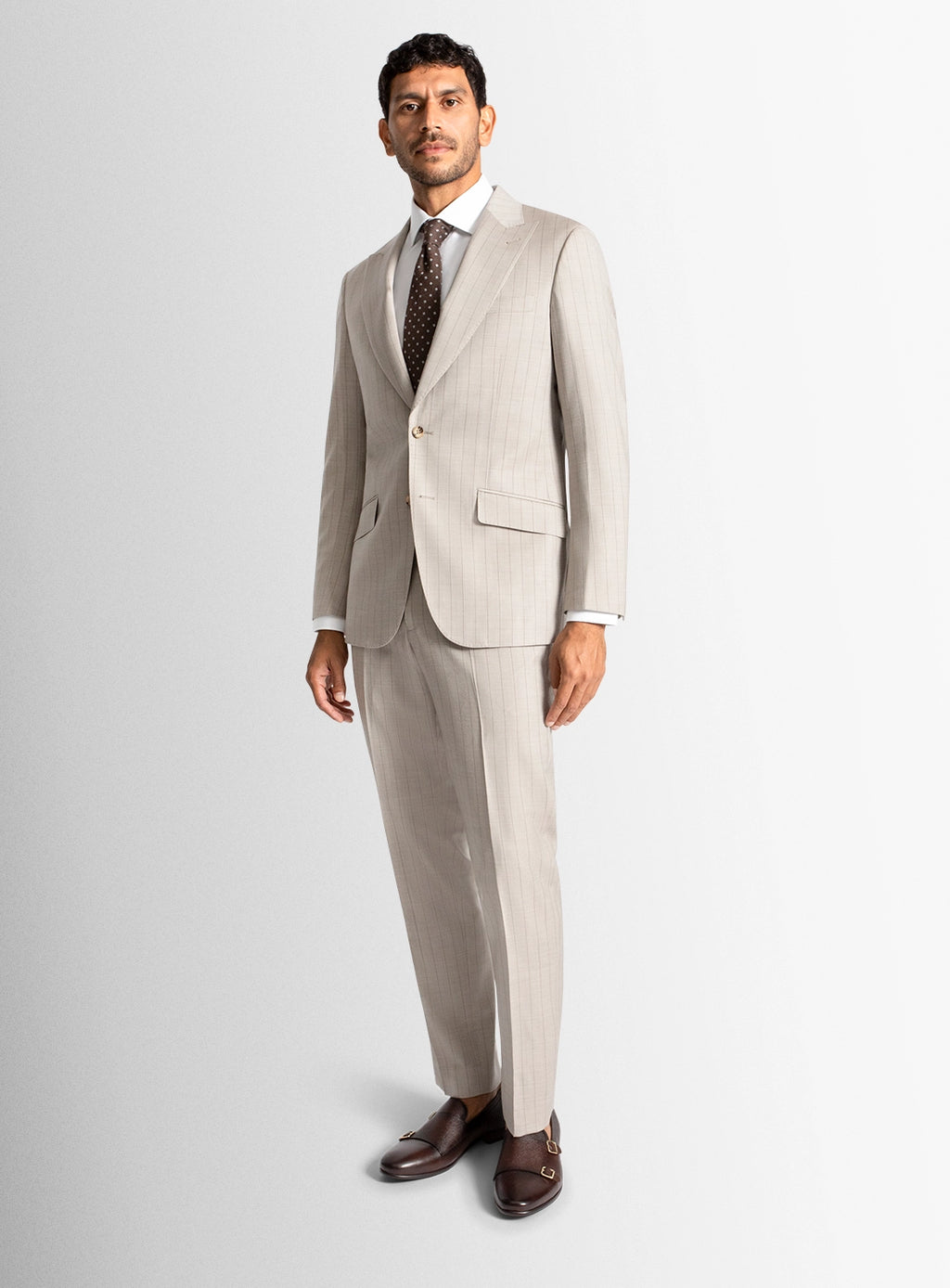 Man wearing a beige suit with a white shirt and brown shoes on a light gray background
