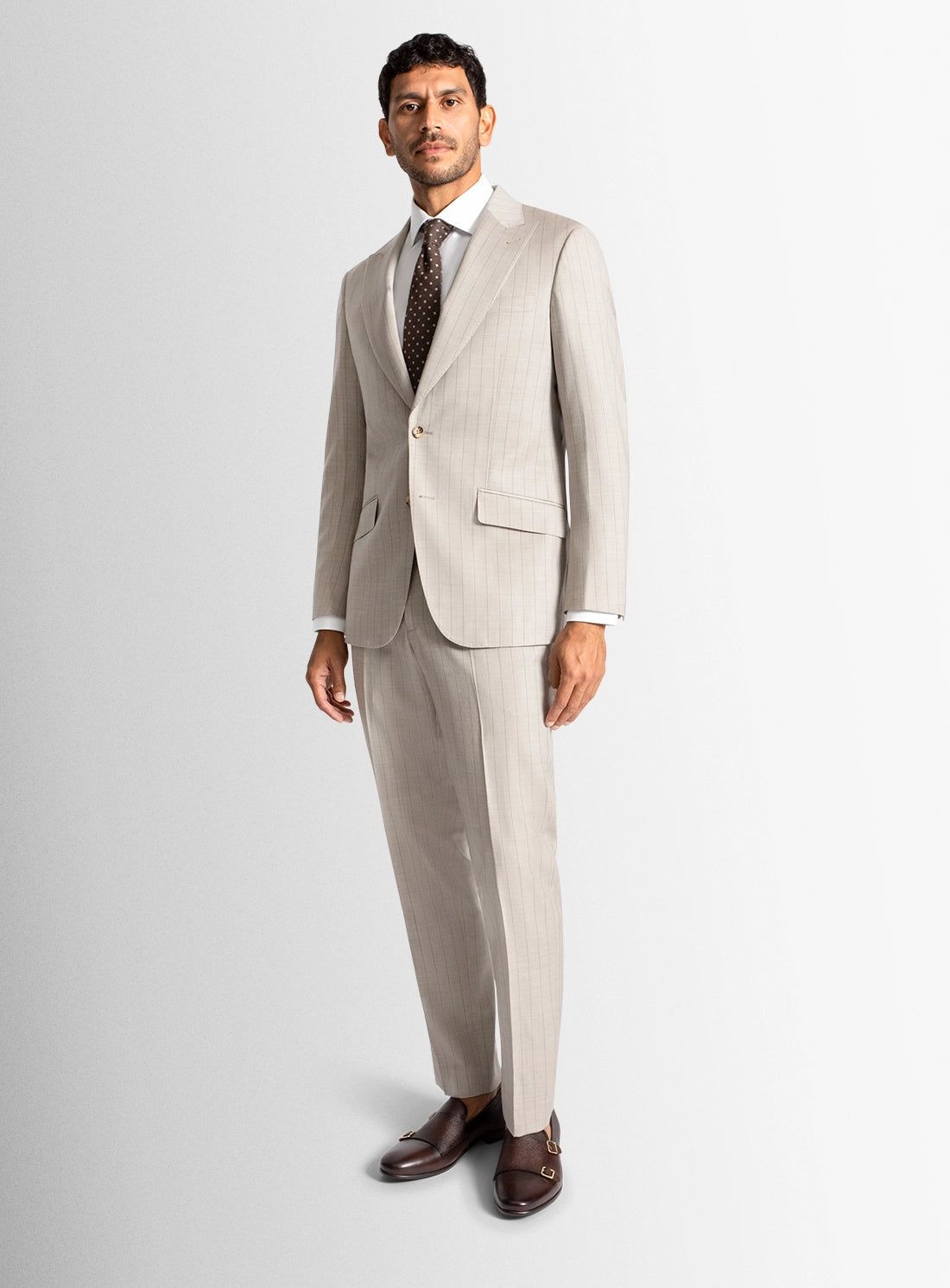 Man wearing a beige suit with a white shirt and brown shoes on a light gray background