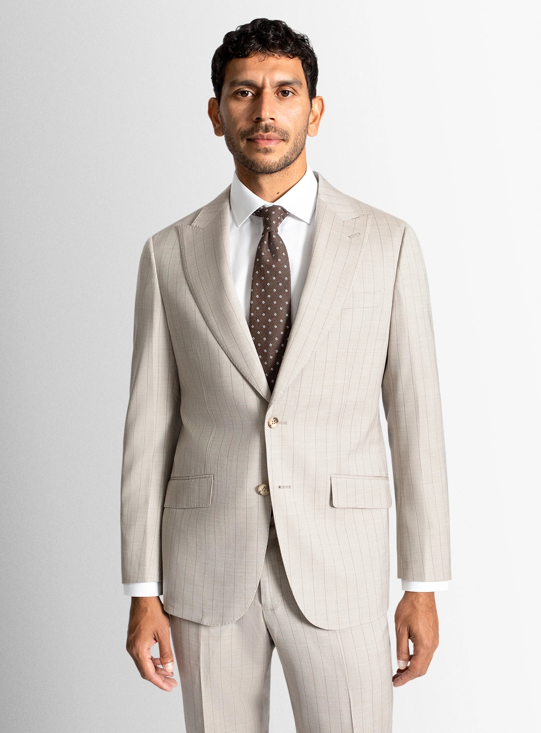 Man wearing a beige suit with a white shirt and patterned tie on a light gray background