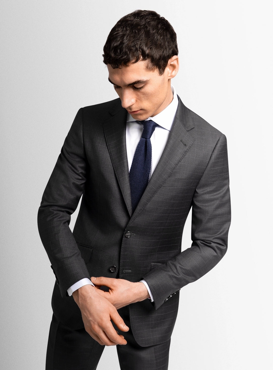 Man wearing a gray suit with a white shirt and dark tie on a light gray background