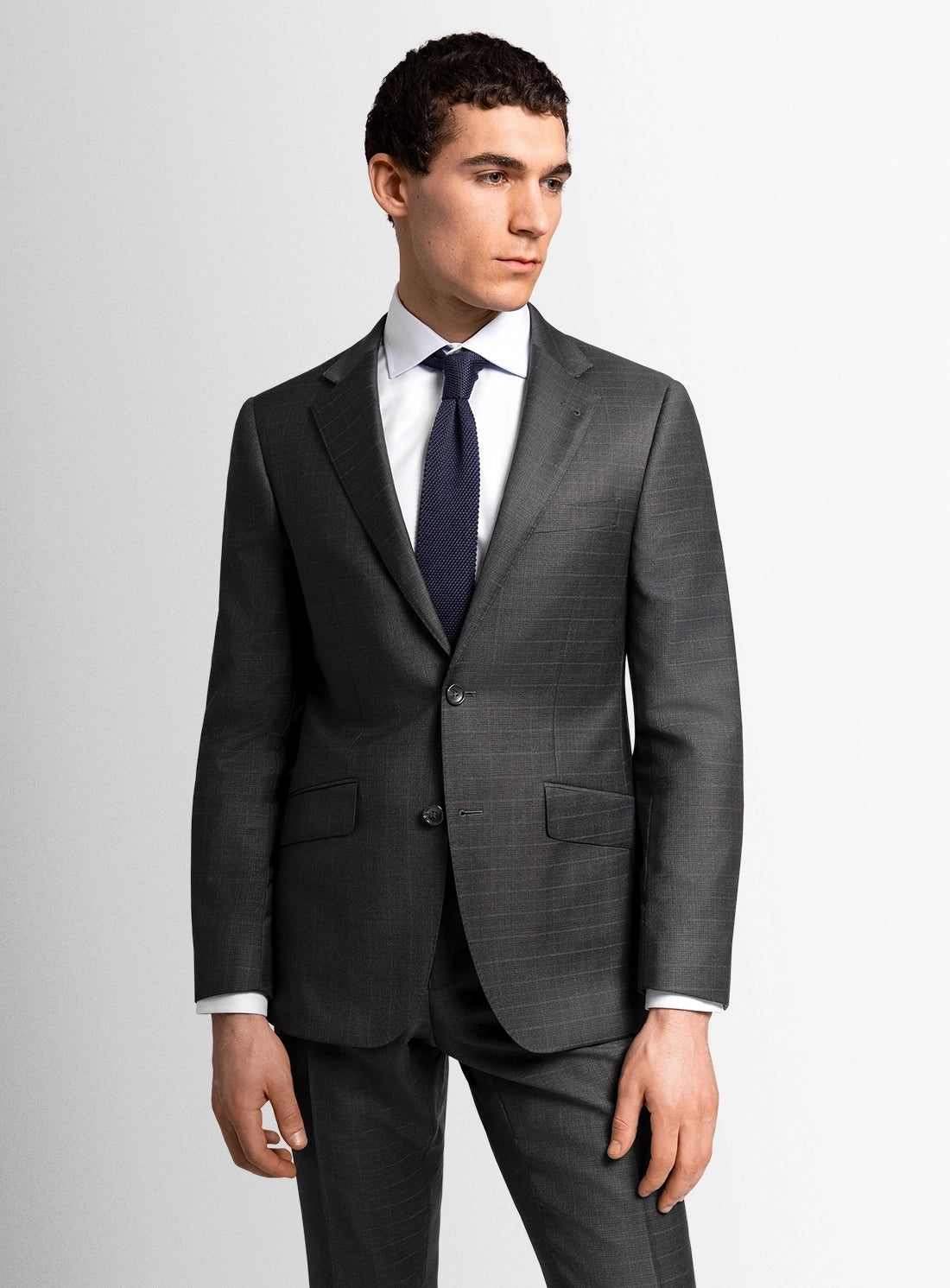 Man wearing a gray suit with a white shirt and dark tie on a light gray background