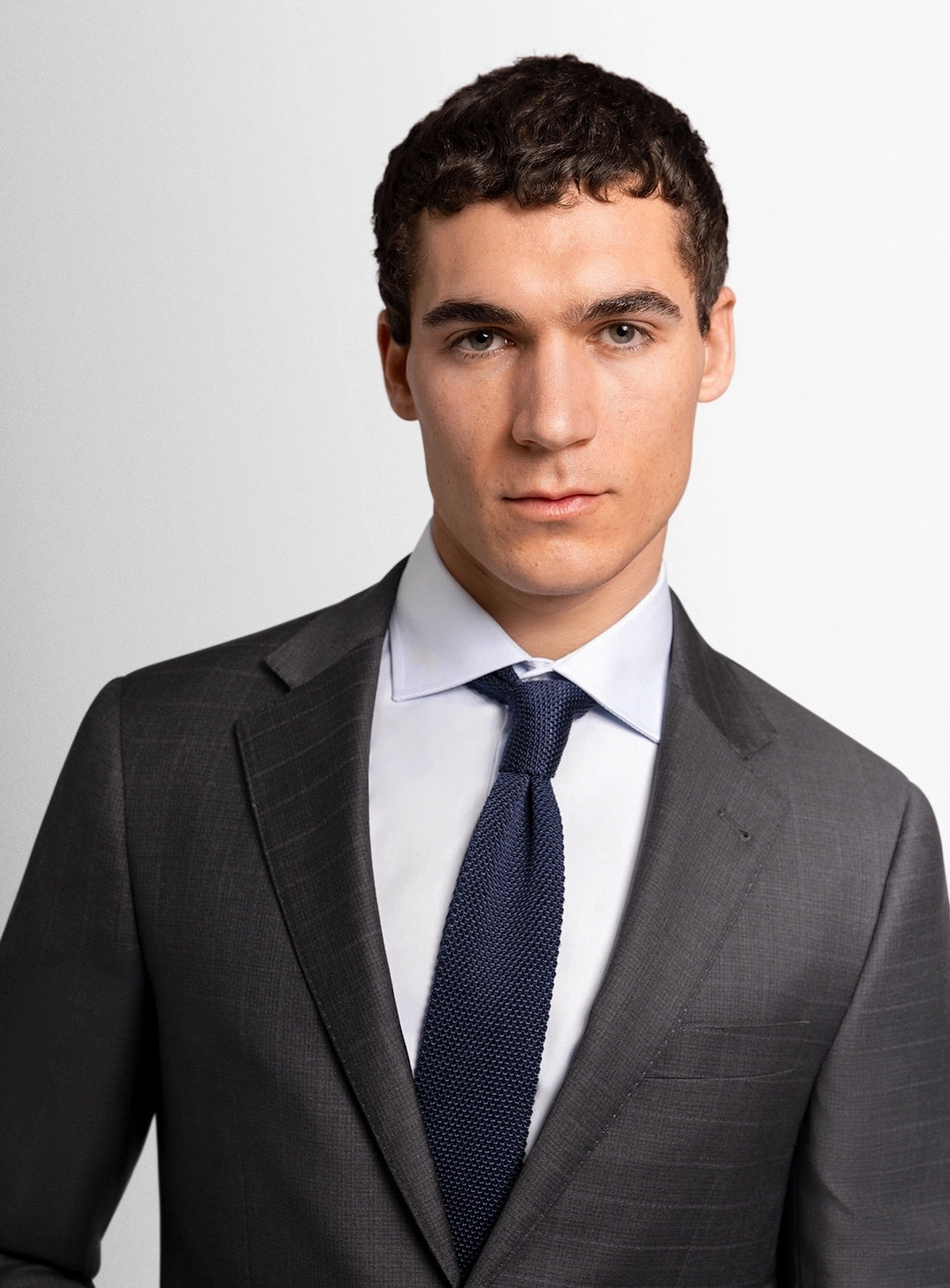 Man wearing a gray suit with a blue tie against a plain background