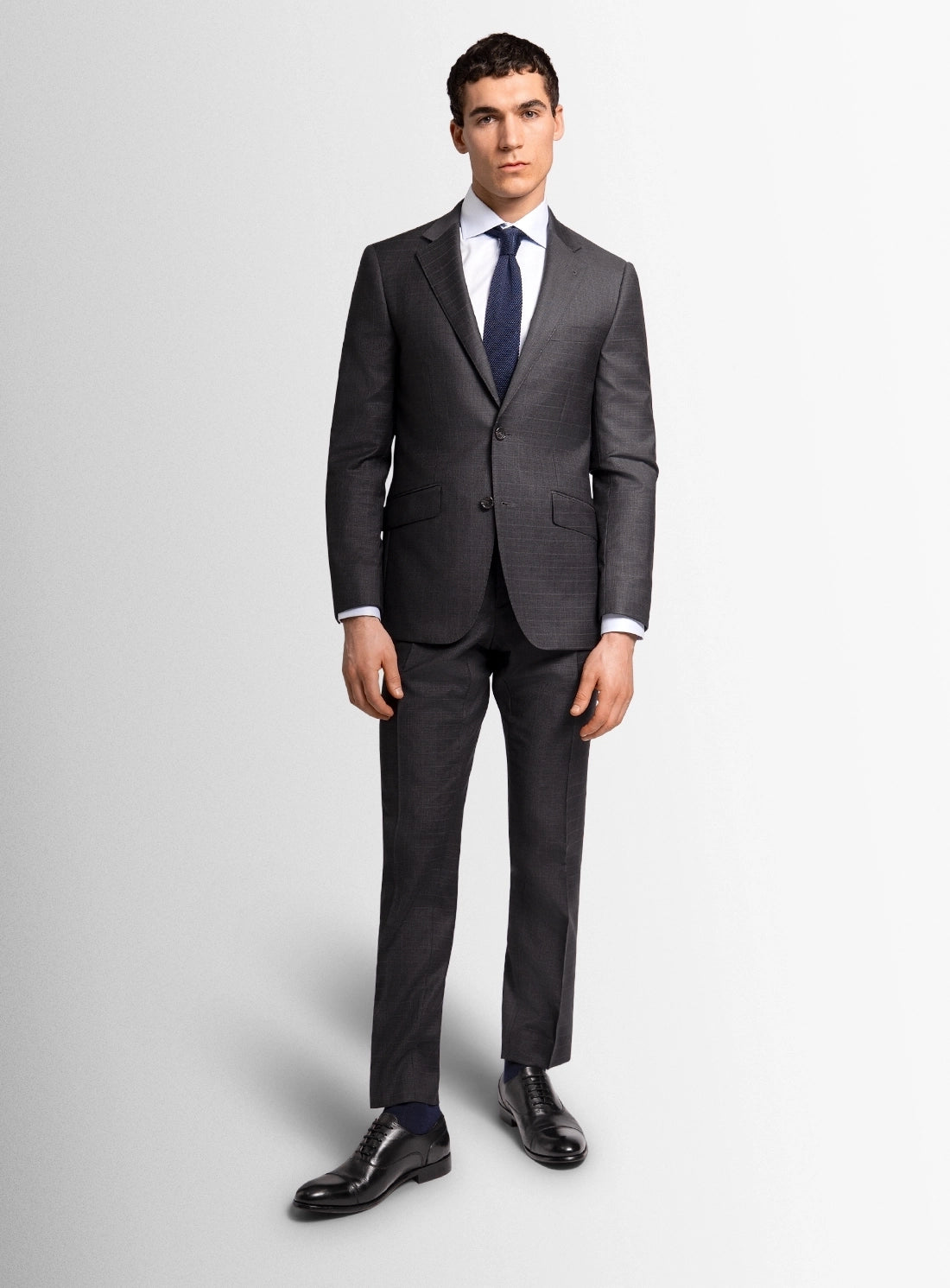 Man wearing a gray suit with a white shirt and blue tie on a light gray background