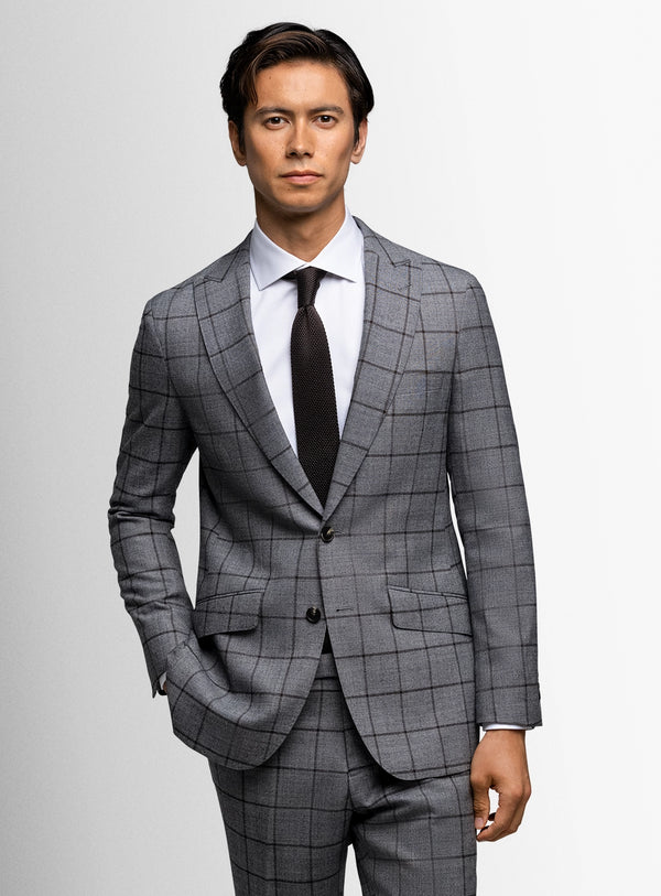 Man wearing a gray checkered suit with a white shirt and black tie on a light gray background
