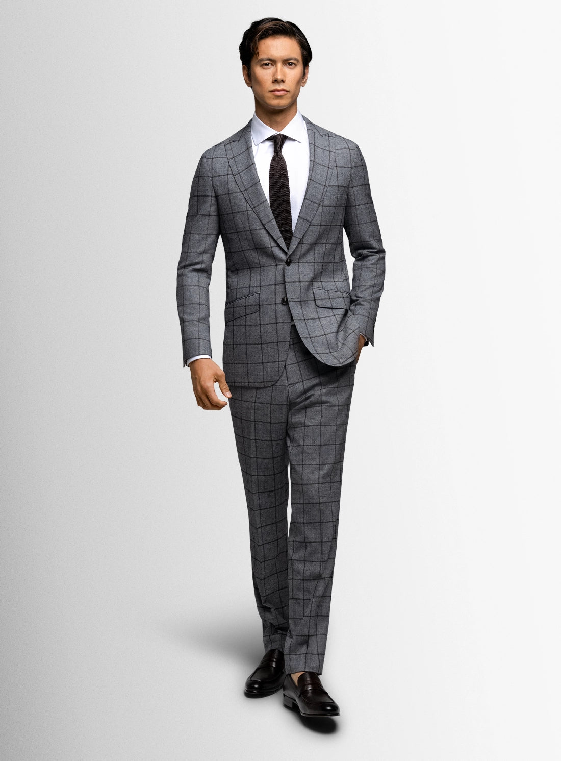 Man wearing a gray checkered suit with a white shirt and black tie on a light gray background