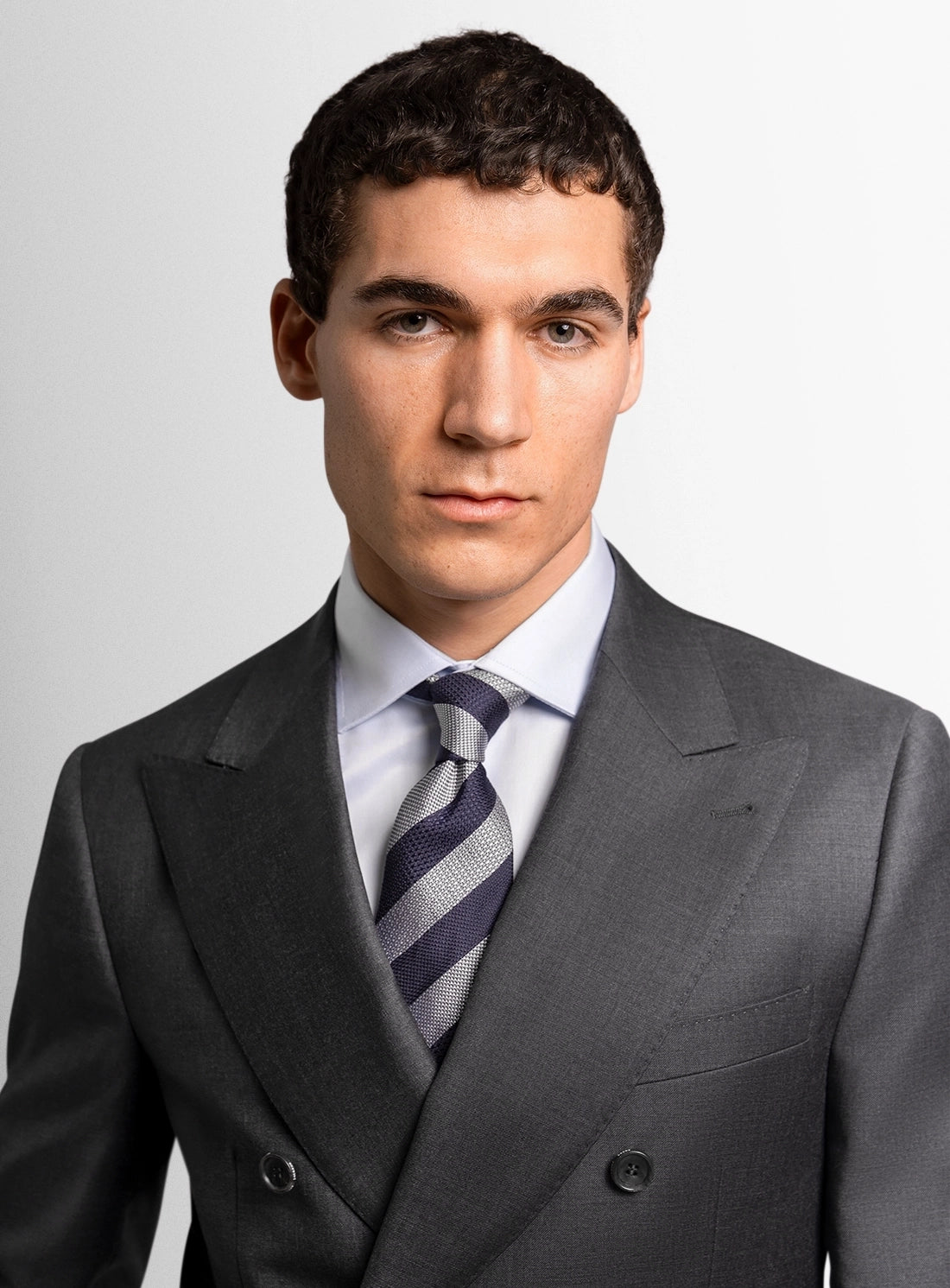 Man wearing a gray suit with a blue tie against a plain background