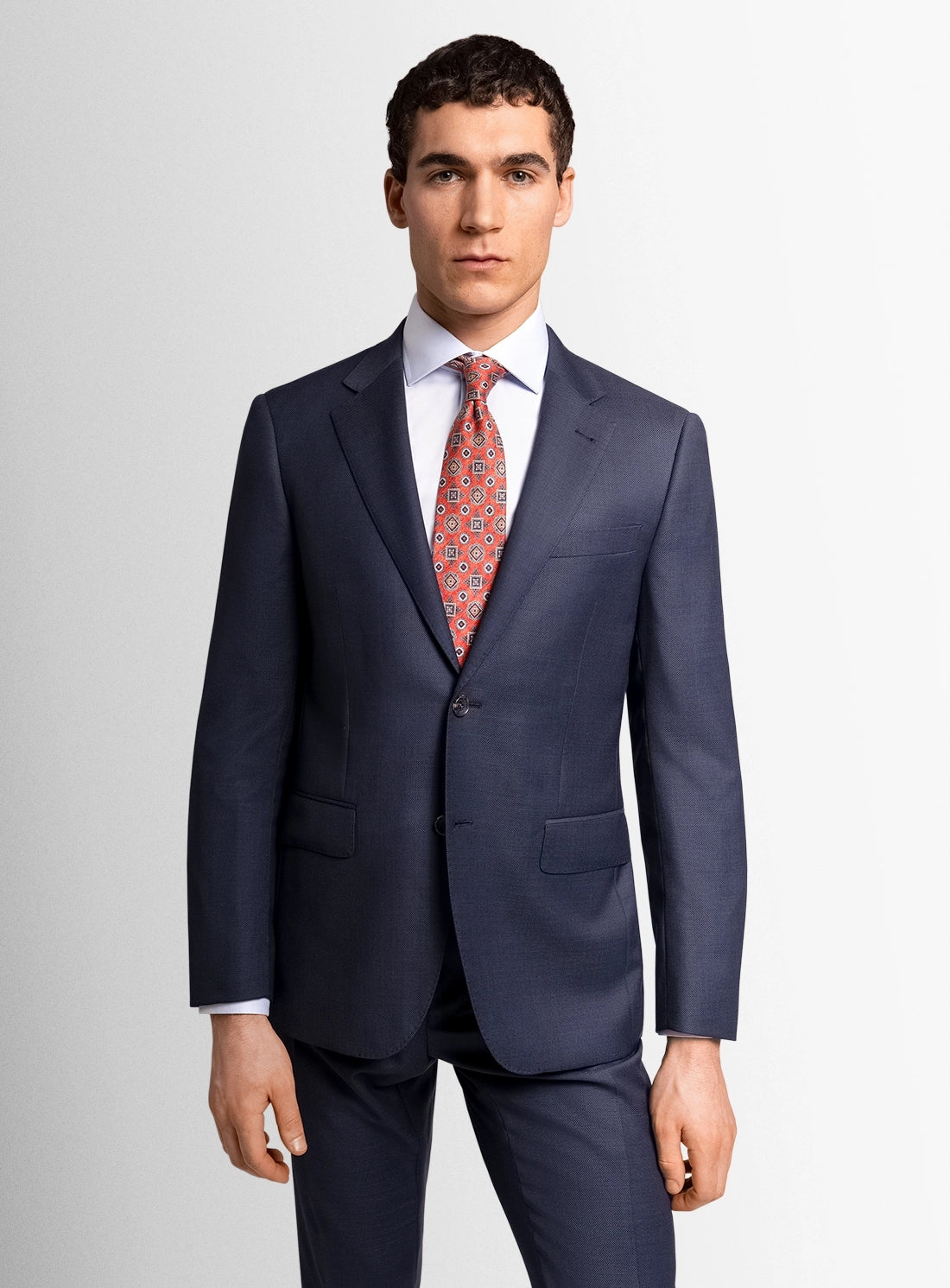 Man wearing a navy suit with a red patterned tie on a light gray background