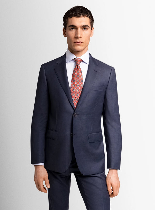 Man wearing a navy suit with a red patterned tie on a light gray background
