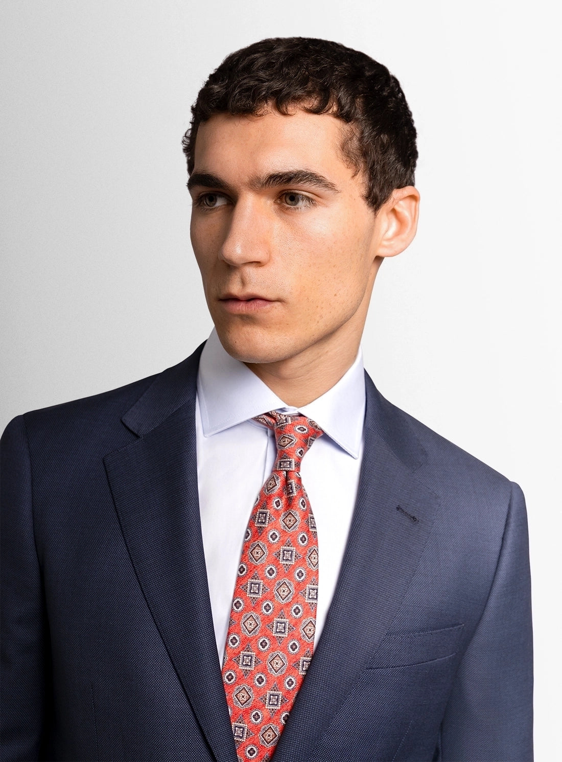 Man wearing a navy suit with a red patterned tie on a white background