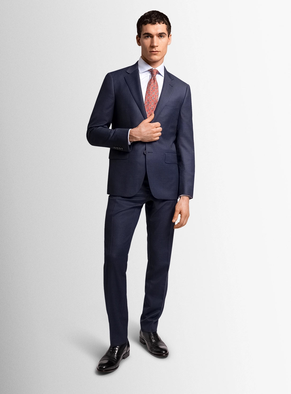 Man wearing a navy suit with a white shirt and red tie on a light gray background